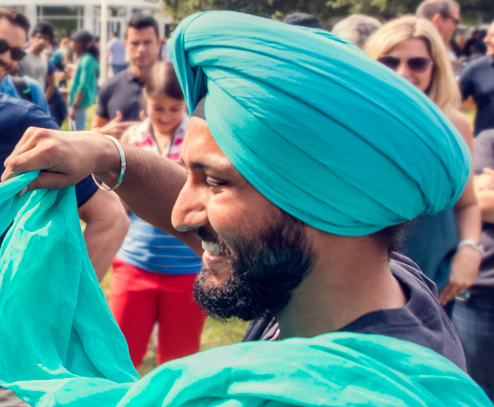 Foto de un hombre con un turbante, sonriendo mientras le pone un turbante a otra persona.