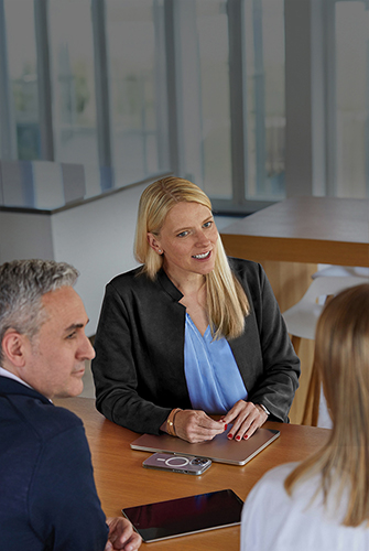 Drie leden van het Sales & Business Development-team van Apple zitten in een gemeenschappelijke ruimte aan een tafel te praten.