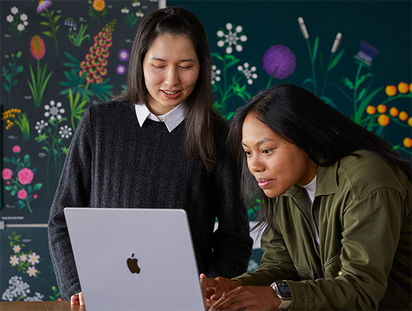 Dos personas del equipo de marketing de Apple trabajan juntas en un MacBook frente a unos carteles que ha diseñado su equipo.