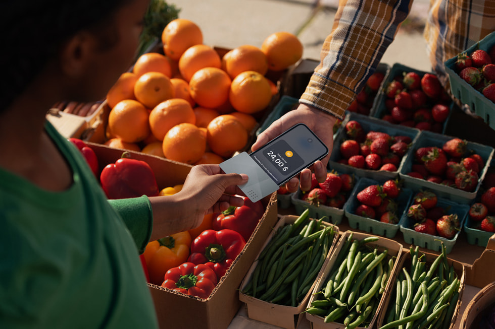 Un client tient son iPhone à côté de celui d’un commerçant pour conclure sa transaction dans un marché fermier.