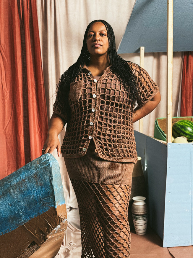 A portrait of designer Nia Thomas wearing a crocheted brown skirt and matching top, against a backdrop made to look like a fruit stand. Shot on iPhone 16 Pro Max by Karston Tannis.