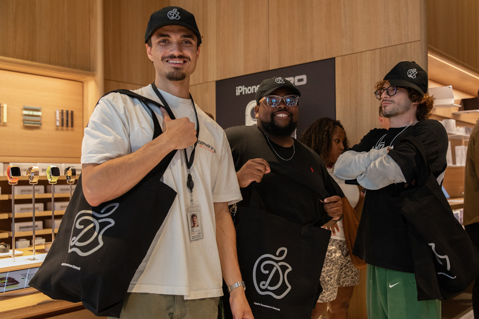 Customers pose with tote bags and hats celebrating the opening of Apple Downtown Detroit.