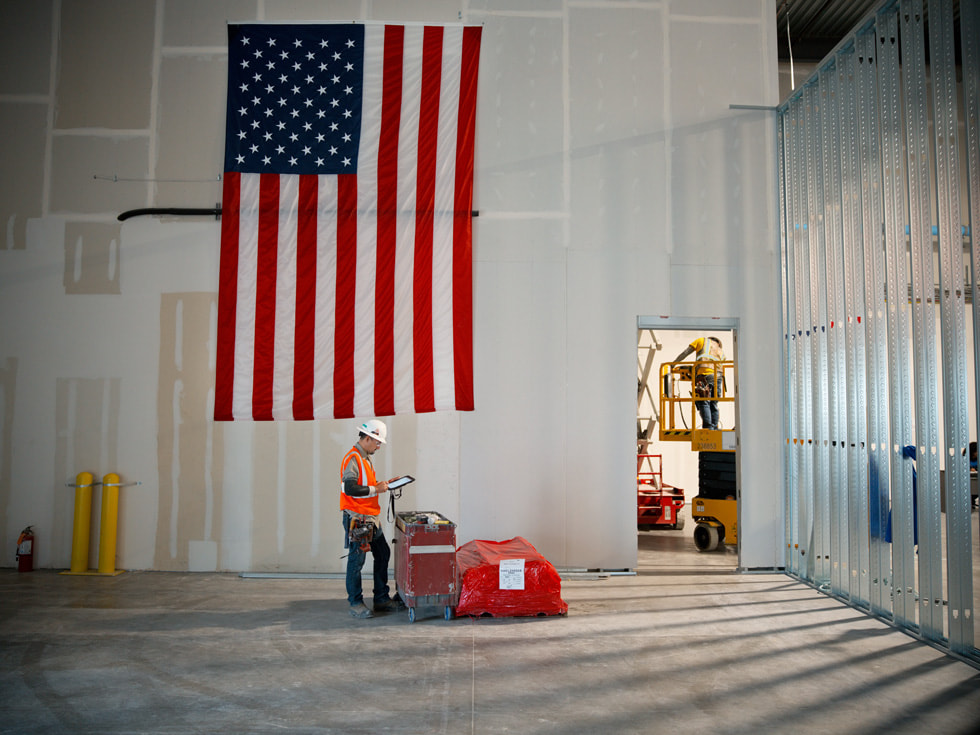 A worker stands in front of a large American flag inside the under-construction Apple Advanced Manufacturing Center in Houston.
