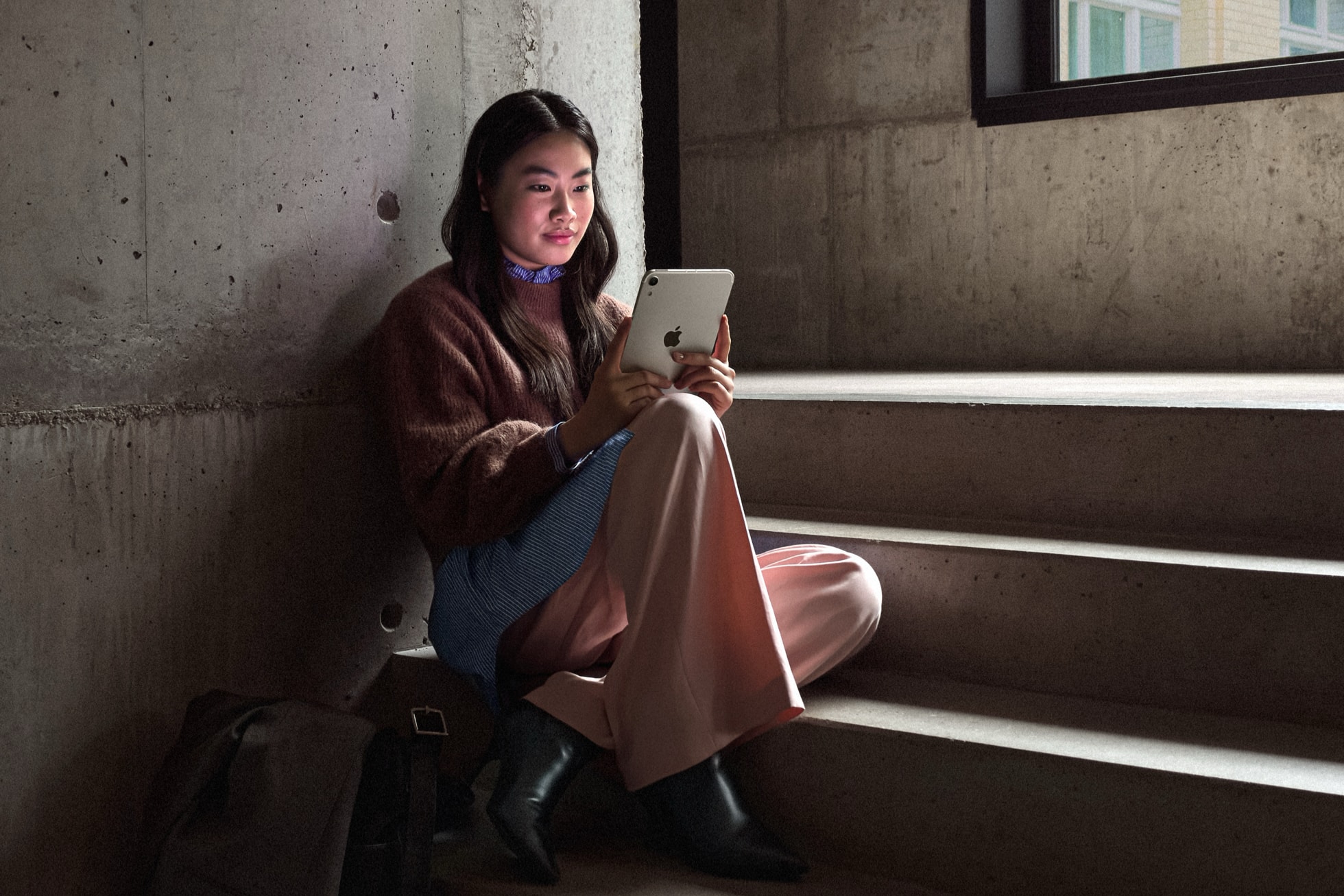 A person sits on stairs while holding iPad mini.