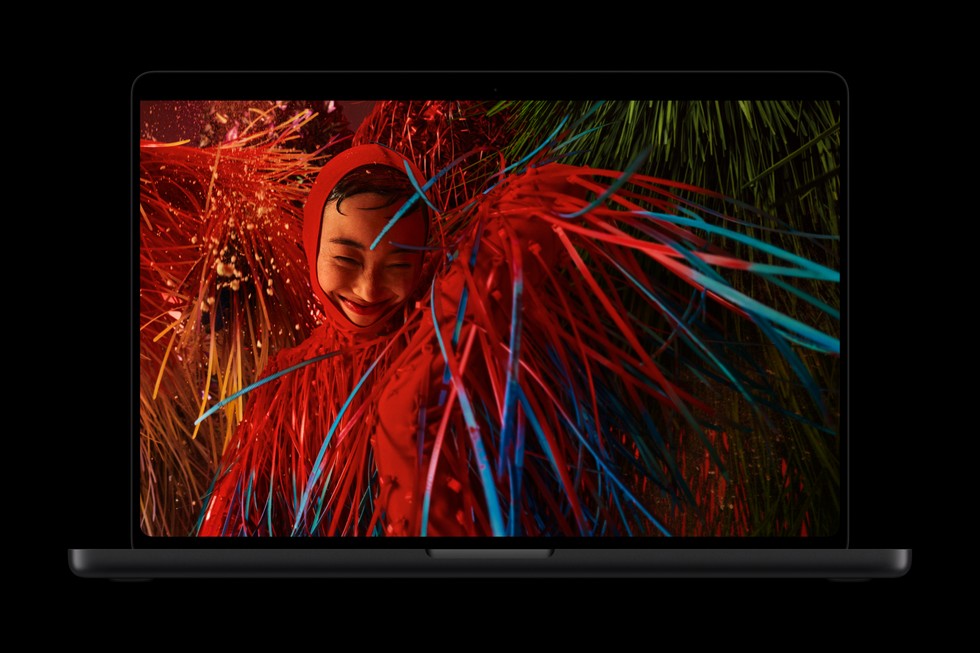 An open MacBook Pro with PROLED XDR Display shows a person dressed in a vibrant red costume.