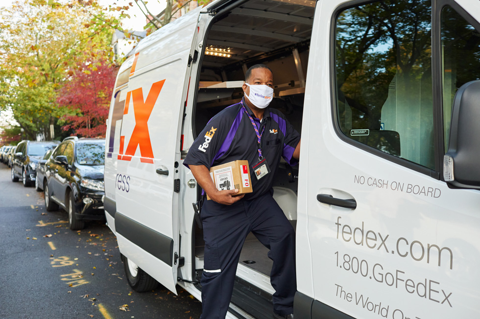 A FedEx worker delivers an Apple package from a FedEx delivery van.