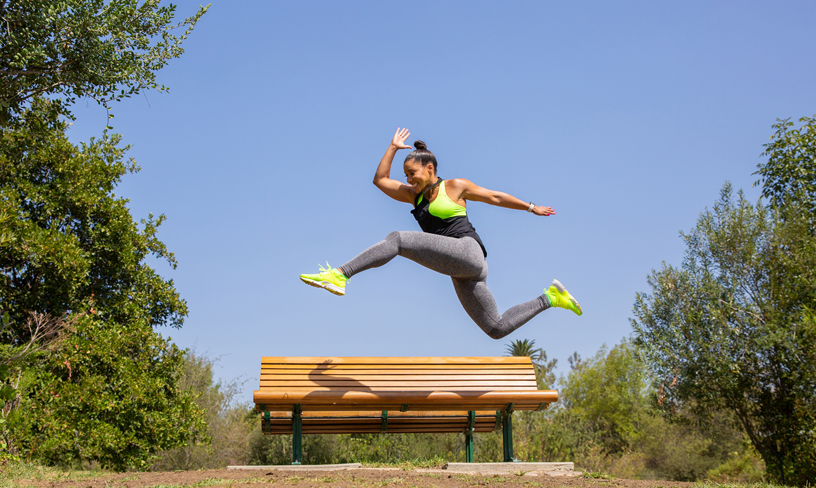 Celebrity fitness trainer Jeanette Jenkins jumping over a bench.
