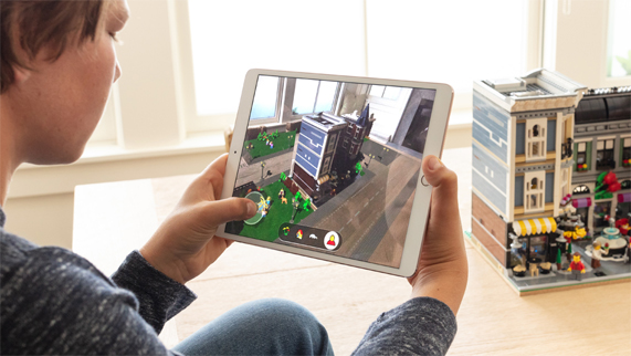 Boy sitting in front of a LEGO building in a room, holding an iPad with LEGO AR City on the screen.