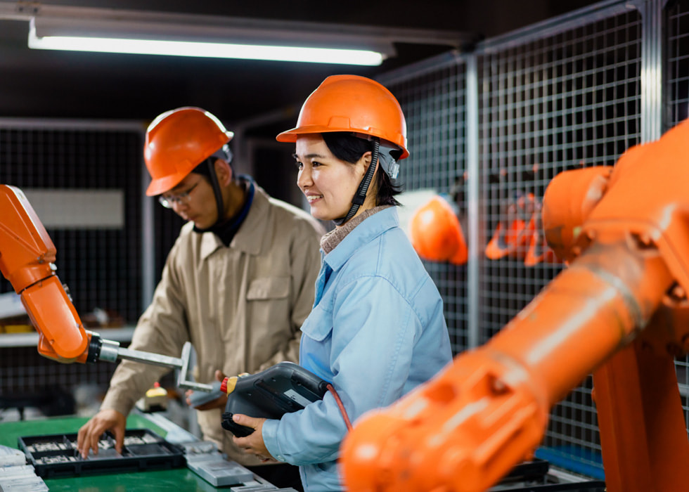 Two people in hard hats work in a lab setting.