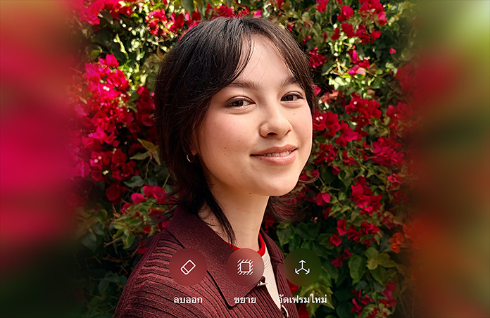 รูปภาพบุคคลที่มีผมสีน้ำตาลกำลังยิ้มแย้ม, สวมเสื้อสเวตเตอร์สีน้ำตาล, ล้อมรอบด้วยดอกไม้สีแดง, การสาธิตการปรับแต่งภาพถ่ายด้วย AI พร้อมตัวเลือกในการลบออก, ขยาย และจัดเฟรมใหม่ที่แสดงอยู่เหนือภาพ