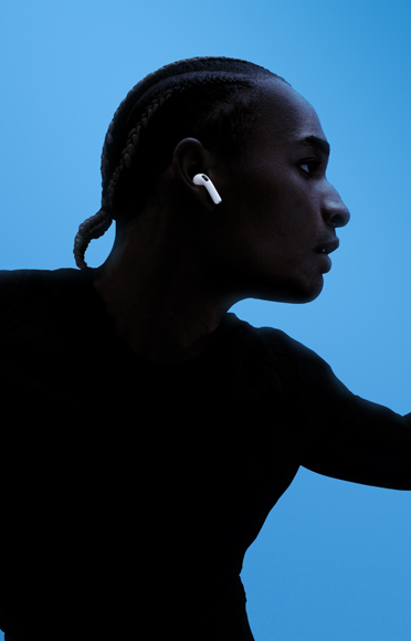 A person wearing AirPods&nbsp;5, arms spread, coloured background