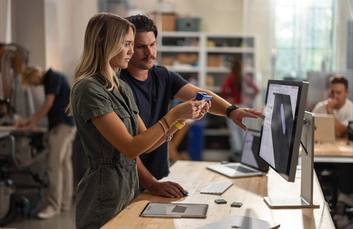 Dos estudiantes colaboran con un modelo de un componente real mientras observan un proyecto en 3D en un monitor Studio Display para el Mac, sobre la mesa hay un MacBook, un Apple Pencil y un iPad