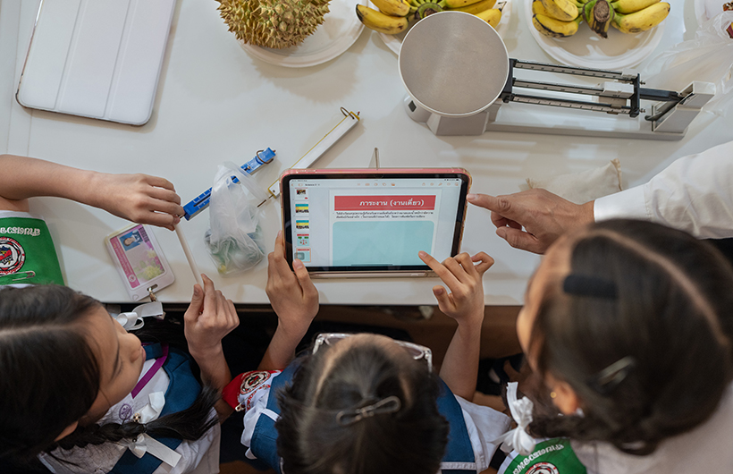 iPadを囲み、理科のプロジェクトのプレゼンテーション資料を共同作業で作成している3人の小学生