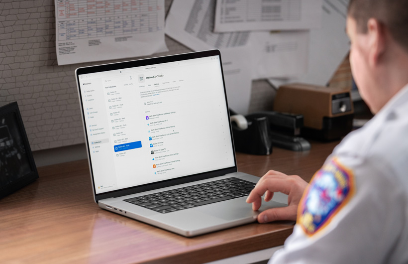 Un membro del gruppo di comando dei vigili del fuoco è seduto in ufficio e ha un MacBook con Apple Business Essentials in evidenza sullo schermo