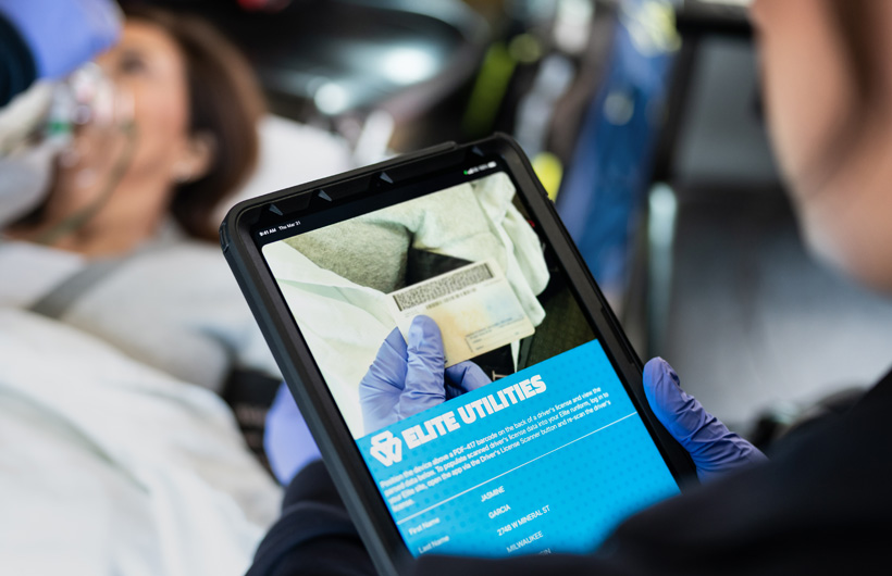 L’app Elite Utilities è aperta su un iPad mentre un paramedico scansiona la patente di guida di una donna stesa su una barella