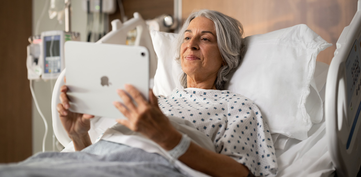 En kvinnlig patient ligger i en sjukhussäng och tittar på en iPad.