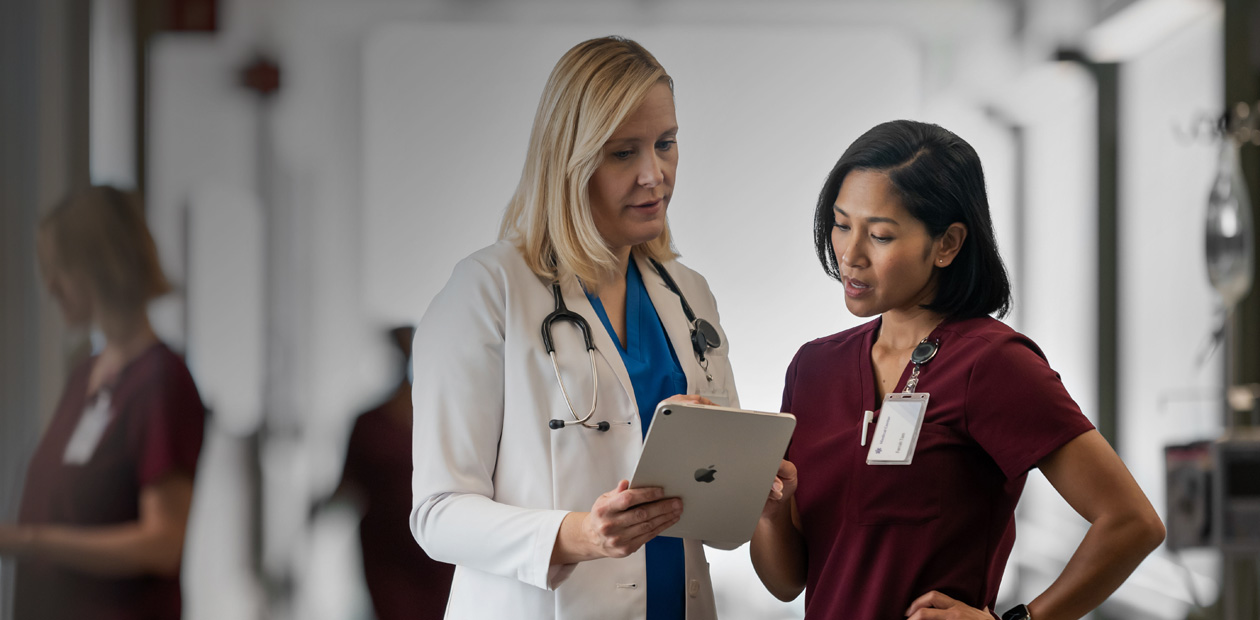 A doctor and a nurse looking at an iPad together in a hospital hallway.