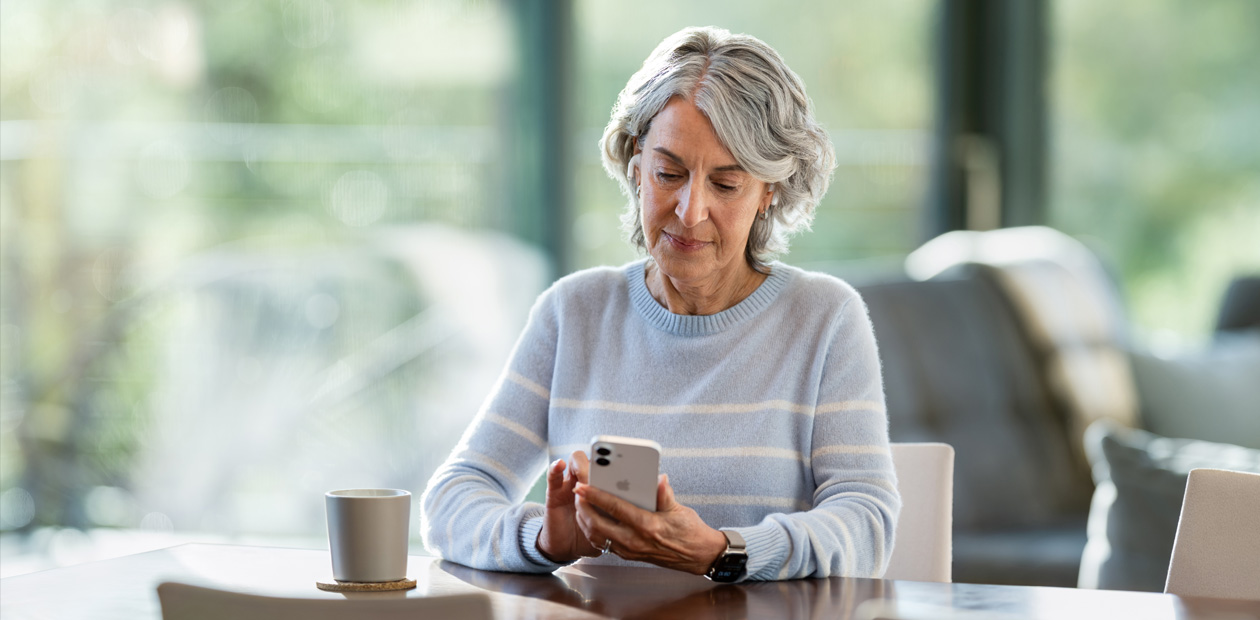 Une femme âgée, assise à une table, regarde un iPhone.