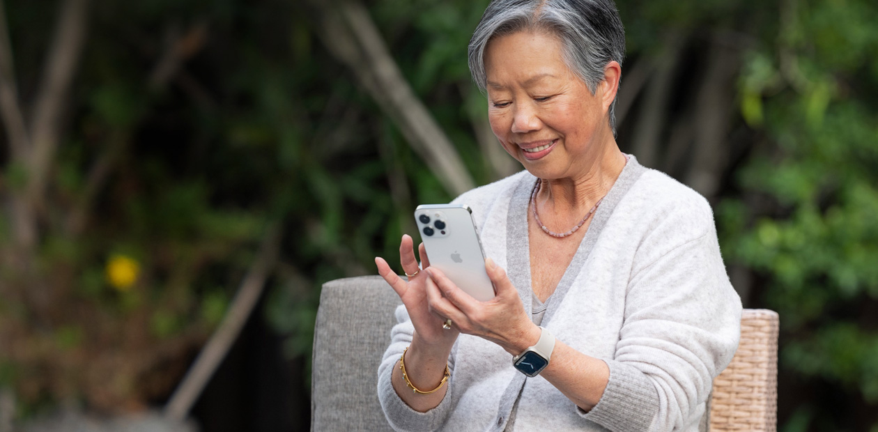 Une femme âgée, assise sur une chaise, regarde un iPhone.