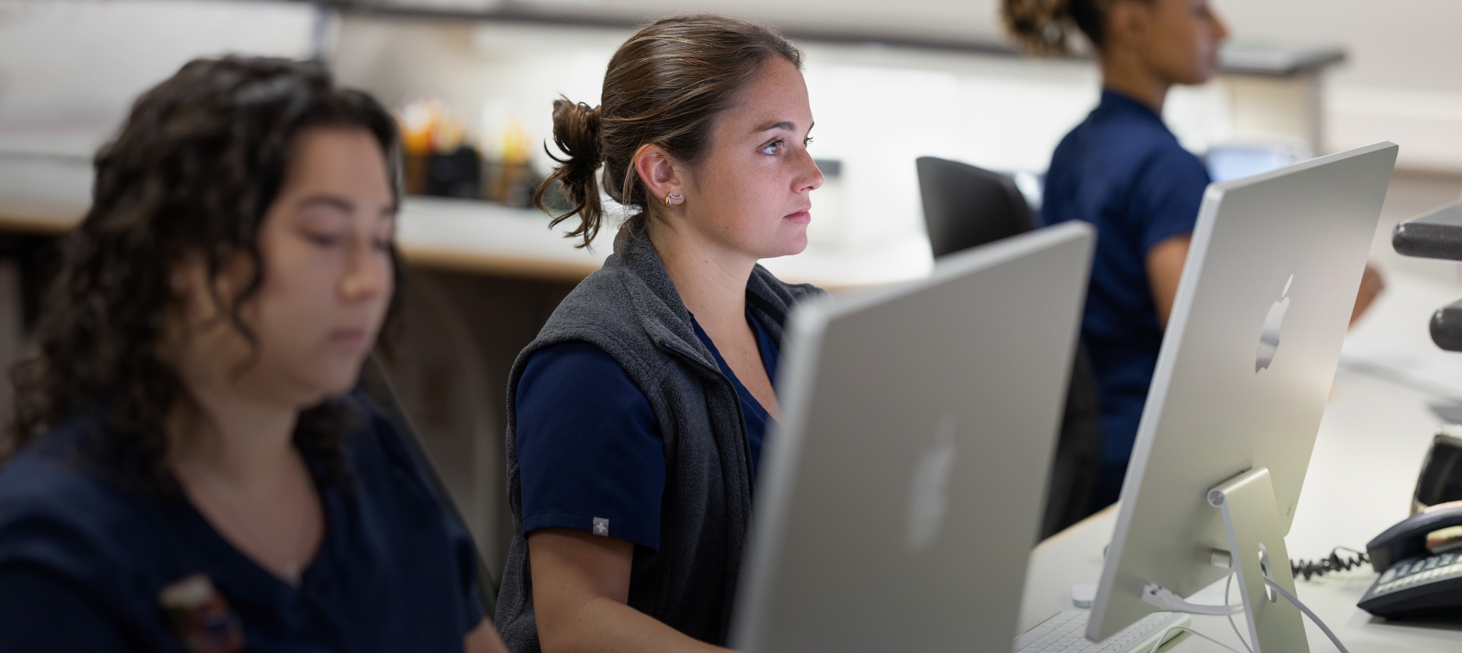 Three nurses working behind iMac screens.